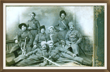 Черняевские казаки, вернувшиеся с фронта 1-й Мировой войны. Благовещенск, 1918 г.   Фотопортрет групповой (8 чел.) наклеен на паспарту серого цвета с рельефным растительным орнаментом. На фоне стены, на полу свободно размещены портретируемые в 3 ряда. В 1-м ряду два чел., полулежа, оперевшись  на одну руку. Перед ними на полу лежит голова животного со скрещенными на ней двумя шашками. Во 2-м ряду – четверо сидят. В 3-м ряду – двое стоят. Все мужчины одеты в военную казачью форму –шинели, сапоги, папахи.